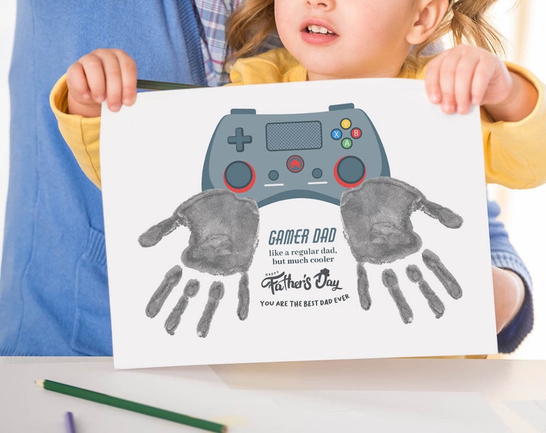 K&ouml;nnte beinhalten: Eine wei&szlig;e Karte mit einem grauen Handabdruck und dem Text "GAMER DAD like a regular dad, but much cooler Father's Day YOU ARE THE BEST DAD EVER". Ein grauer Videospiel-Controller befindet sich &uuml;ber dem Handabdruck.