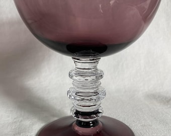 May include: A vintage-style, stemmed glass with a wide, shallow bowl in a deep purple hue. The stem is clear, featuring a stacked, ringed design, and the base is a matching purple. This elegant glassware is suitable for serving cocktails or desserts.