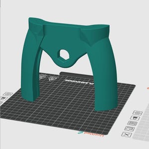 Puede incluir: Un objeto de color turquesa impreso en 3D con dos brazos curvos y un agujero en el centro. El objeto está sobre una superficie de cuadrícula negra y blanca.