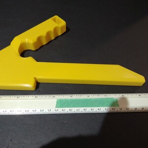 May include: A yellow plastic tool with a handle and a flat, angled blade. The tool is about 7 inches long.