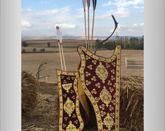 Könnte beinhalten: Zwei verzierte Bogenköcher mit aufwendigen goldenen Stickereien auf einem burgunderfarbenen Hintergrund. Die Köcher sind aus Leder und haben ein traditionelles Design. Die Köcher sind mit Pfeilen mit roten, weißen und schwarzen Befiederungen gefüllt.
