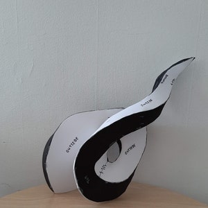 Può includere: Una scultura di carta bianca e nera di una striscia di Möbius con le parole "esterno", "interno", "alto" e "girando" scritte su di essa.