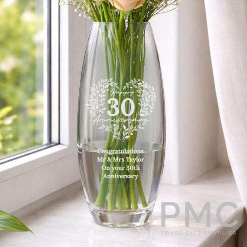 May include: A clear glass vase featuring an etched design of a heart-shaped wreath surrounding the text Happy 30 Anniversary. Below the wreath, the text reads Congratulations Mr & Mrs Taylor On your 30th Anniversary. The vase holds green stems.