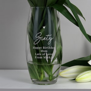 May include: A clear glass vase with a heart and the text "Sixty Happy Birthday Mum Lots of Love From Mark x" engraved on the side. The vase is filled with water and green stems.