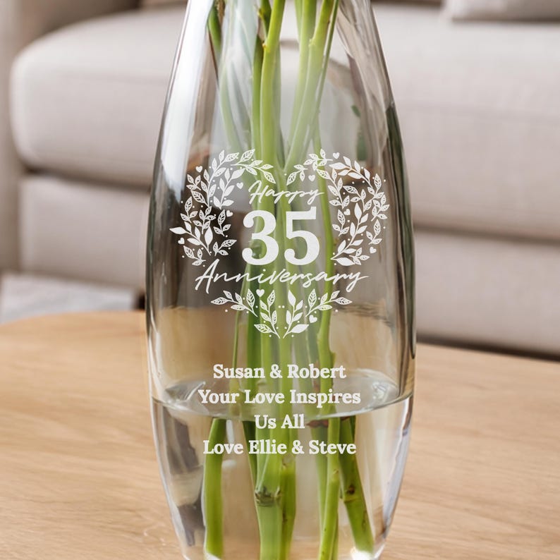May include: A clear glass vase featuring a white etched design of a heart made of leaves surrounding the text Happy 35 Anniversary. Below this, the text reads Susan & Robert, Your Love Inspires Us All, and Love Ellie & Steve.