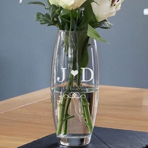 May include: A clear glass vase with a personalised inscription. The inscription reads "J ♥ D 14.12.2022" with a decorative swirl design. The vase is filled with water and white flowers.