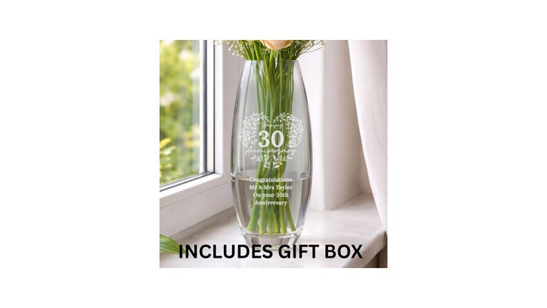 May include: A clear glass vase with a tapered oval shape, featuring an etched heart-shaped wreath design surrounding the number 30. Below the wreath, the text reads: Congratulations Mr & Mrs Taylor On your 30th Anniversary. Green flower stems are visible inside.