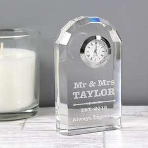 May include: A clear glass clock with a silver face and black Roman numeral hour markers. The clock is engraved with "Mr & Mrs TAYLOR EST. 2018 Always Together".
