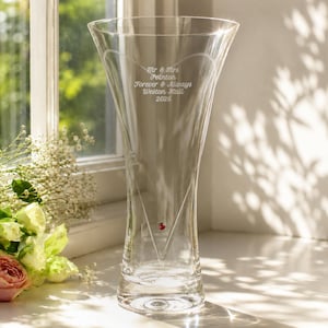 May include: A clear glass vase with a flared rim and a tapered base. The front features an etched heart outline, a small red crystal accent, and the engraved text: Mr & Mrs Pointon, Forever & Always, Weston Hall, 2026. The vase has a smooth finish.