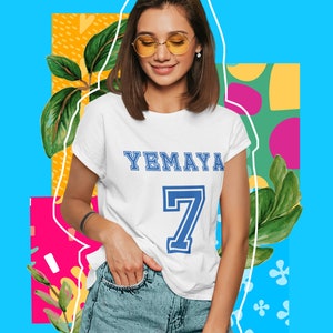 Puede incluir: Una camiseta blanca con el texto "YEMAYA 7" impreso en azul en la parte delantera. La persona que lleva la camiseta también lleva pantalones cortos de mezclilla y gafas de sol amarillas.