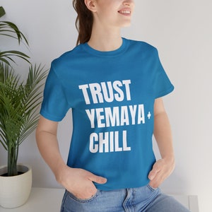 Puede incluir: Una camiseta azul turquesa con el texto "TRUST YEMAYA + CHILL" impreso en blanco.