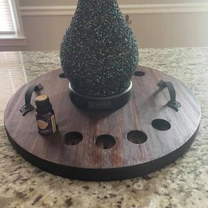 May include: A round wooden tray with a black rim and two leather handles. The tray has eight holes for essential oil bottles. A black Scentsy diffuser with a sparkly black glass shade sits on the tray. A small bottle of essential oil is in one of the holes.