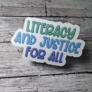 May include: A white sticker with the text "Literacy and Justice for All" in a rainbow gradient of blue, green, and purple.