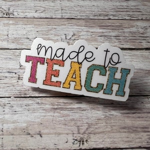 May include: A white sign with the text "made to TEACH" in black script. The word "TEACH" is in colorful block letters with gold glitter accents.