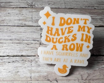 May include: A white sticker with orange text that reads "I DON'T HAVE MY DUCKS IN A ROW. I HAVE SQUIRRELS AND THEY ARE AT A RAVE." A small orange duck graphic is at the bottom.