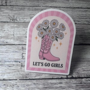 May include: A pink sticker with a pink cowboy boot filled with daisies. The sticker has a pink and white striped border and the words "LET'S GO GIRLS" in black text.