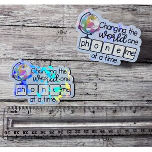 May include: Two iridescent stickers with a globe design and the text "Changing the world one phone me at a time."