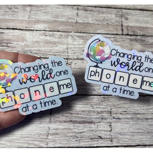 May include: Two iridescent stickers with the text "Changing the world one phoneme at a time." Each sticker features a globe graphic and the word "phoneme" spelled out in individual squares.