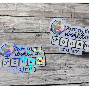 May include: Two iridescent stickers with a globe illustration and the text "Changing the world one phoneme at a time."
