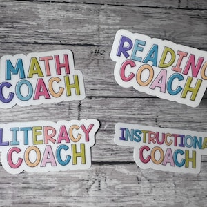 May include: Four colorful stickers with the words "MATH COACH", "READING COACH", "LITERACY COACH", and "INSTRUCTIONAL COACH". Each sticker has a white border and is on a gray wooden surface.