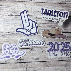 May include: Purple and white stickers with the text "Tarleton University", "Tarleton", "2025 Ring Dunk", and "TSU". There is also a sticker of a cowboy hat with the text "Tarleton" and a sticker of two cowboy boots with stars.
