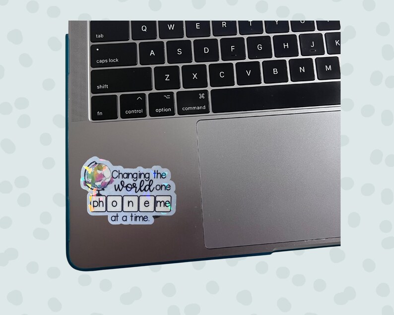 May include: A holographic sticker with a globe illustration and the text "Changing the world one phone me at a time." The sticker is placed on a silver laptop.