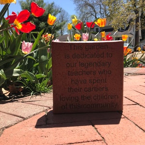 May include: A red brick with the inscription "This garden is dedicated to our legendary teachers who have spent their careers loving the children of this community."