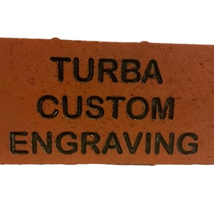May include: A red brick with the text "TURBA CUSTOM ENGRAVING" engraved in black.