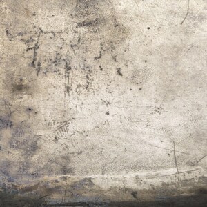 May include: A close-up of a textured, light gray surface with scratches and marks. The surface has a worn and aged appearance.