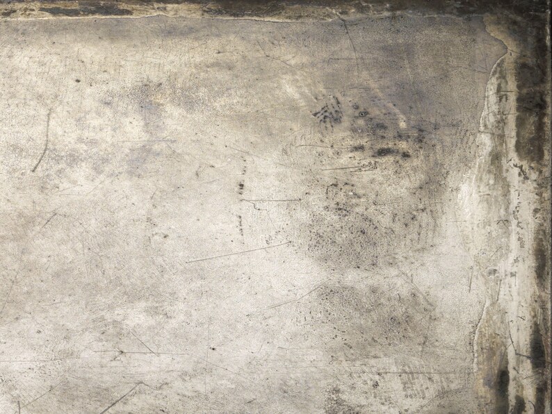May include: A close-up of a textured, metallic surface with scratches and marks. The surface is a light gray color with darker gray streaks and spots.