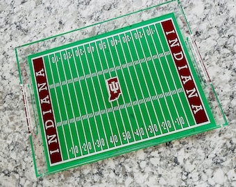 Puede incluir: Una bandeja de servir de acrílico transparente con un diseño de campo de fútbol verde. La bandeja presenta el logotipo de la Universidad de Indiana y las palabras "INDIANA" en ambos lados.