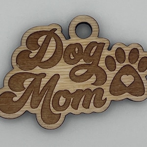 May include: Wooden dog mom ornament with a paw print and a heart. The ornament is brown and has a hole at the top for hanging.