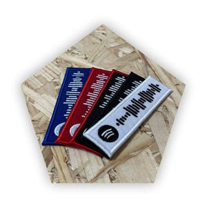 Op de afbeelding: Vijf geborduurde patches met een zwart-witte barcode-ontwerp. De patches zijn in blauw, rood, zwart en wit. De witte patch heeft een kleine witte cirkel met drie zwarte lijnen in het midden.