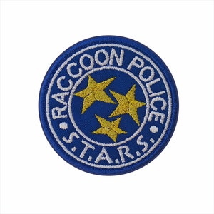 May include: A circular blue embroidered patch with the text "RACCOON POLICE S.T.A.R.S." in white. Three gold stars are in the centre. The patch has a white border.
