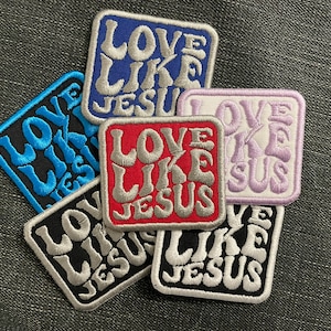 Könnte beinhalten: Sechs gestickte Bügelbilder mit dem Text "Love Like Jesus" in verschiedenen Farben, darunter Blau, Rot, Schwarz und Weiß.