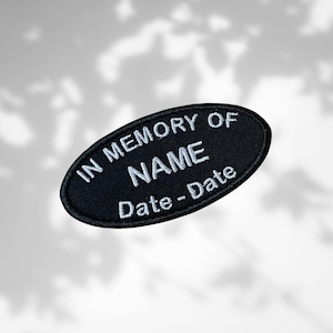 May include: Black oval patch with white embroidered text. The text reads "IN MEMORY OF NAME Date-Date". The patch is likely a memorial item, possibly for clothing or a keepsake.