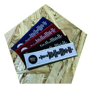 Op de afbeelding: Vijf geborduurde patches met een Spotify-logo en een barcode-ontwerp. De patches zijn in verschillende kleuren: wit, zwart, rood en blauw.