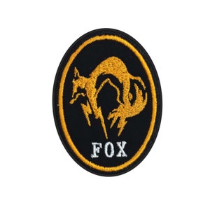 May include: A black and yellow embroidered patch featuring a stylised fox design and the word "FOX" in white lettering.