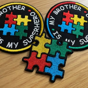 Peut inclure: Deux patchs ronds brodés avec le texte "Mon frère est mon super-héros" et un motif de pièce de puzzle en rouge, jaune, bleu et vert. Un motif de pièce de puzzle séparé en rouge, jaune, bleu et vert.
