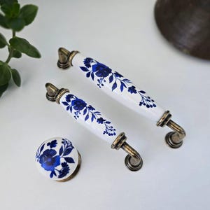 Puede incluir: Juego de herrajes para armarios con motivos florales blancos y azules. El juego incluye dos tiradores y un pomo. Los tiradores miden 15 cm de largo y el pomo tiene un diámetro de 4 cm. Los herrajes tienen un acabado de latón.