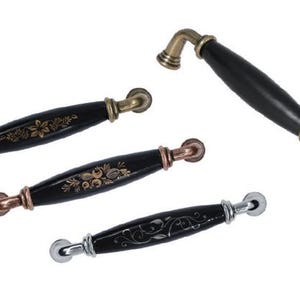 May include: A selection of black cabinet handles with floral and scroll patterns. The hardware has gold, copper, and silver finishes. One larger handle is also present.