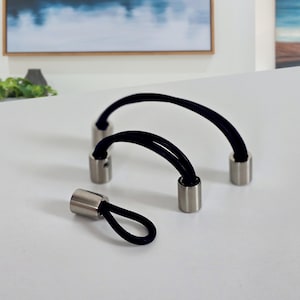 Può includere: Tre elastici per capelli neri con punte in metallo argentato. Gli elastici per capelli sono a forma di curva, con le punte rivolte verso l'esterno. Un elastico per capelli è a forma di anello.