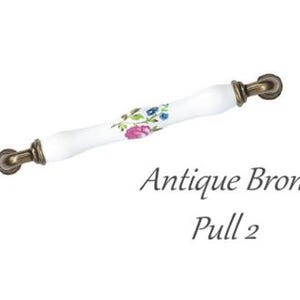 Pode incluir: Puxador de bronze antigo com um centro de cer&acirc;mica branca. A sec&ccedil;&atilde;o de cer&acirc;mica &eacute; decorada com um padr&atilde;o floral em rosa, azul e verde. O texto "Antique Bronze Pull 2" est&aacute; por baixo.