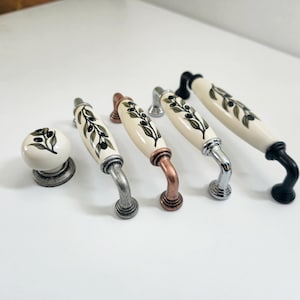 Peut inclure: Cinq boutons de porte en céramique avec des motifs de branches d'olivier. Les boutons sont en différentes finitions, notamment noir, argent, cuivre et argent antique. Un bouton est un bouton rond plus petit.