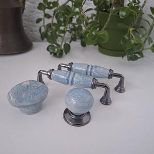Puede incluir: Un conjunto de herrajes para armarios con dos tiradores, un pomo y un tirador. Los tiradores y el pomo tienen un diseño moteado azul claro con detalles metálicos plateados. El tirador tiene un diseño similar. Para la decoración del hogar.