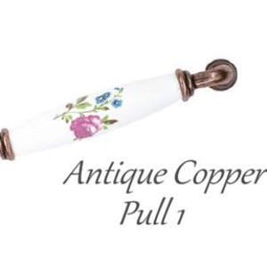 Pode incluir: Puxador de arm&aacute;rio em cobre antigo com centro em cer&acirc;mica branca. A cer&acirc;mica &eacute; decorada com um padr&atilde;o floral em rosa, azul e verde. O texto "Antique Copper Pull 1" est&aacute; abaixo.