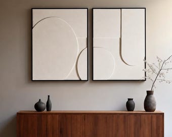 May include: Two framed abstract wall art pieces with black frames, featuring off-white geometric designs. Below, a wooden cabinet with a warm brown finish holds several dark vases and a decorative vase with a branch.