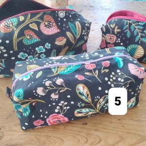 May include: A collection of three floral print cosmetic bags in varying sizes. The bags feature a dark background with colorful botanical patterns, including pink, teal, and gold flowers and leaves. Each bag has a contrasting interior lining and a zipper closure.