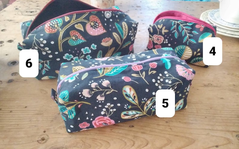 May include: A collection of three floral print cosmetic bags in varying sizes. The bags feature a dark background with colorful botanical patterns, including pink, teal, and gold flowers and leaves. Each bag has a contrasting interior lining and a zipper closure.
