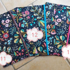 May include: Three fabric-covered notebooks with floral patterns in navy, pink, teal, and gold. Each notebook has a different colored elastic band: brown, teal, and pink. Numbers 11, 12, and 13 are on the notebooks.